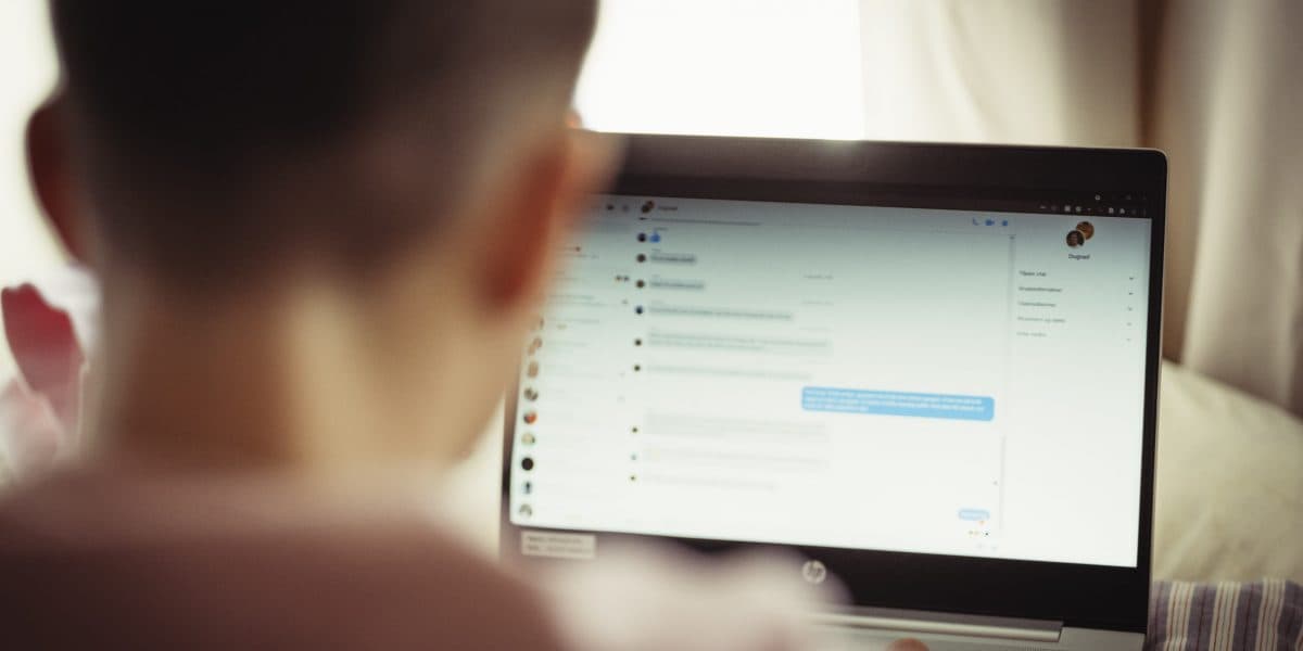 En person sitter foran en bærbar datamaskin og ser på et chatte- eller meldingsprogram med flere synlige samtaler på skjermen. Personens ansikt er ikke synlig, og scenen er svakt opplyst.