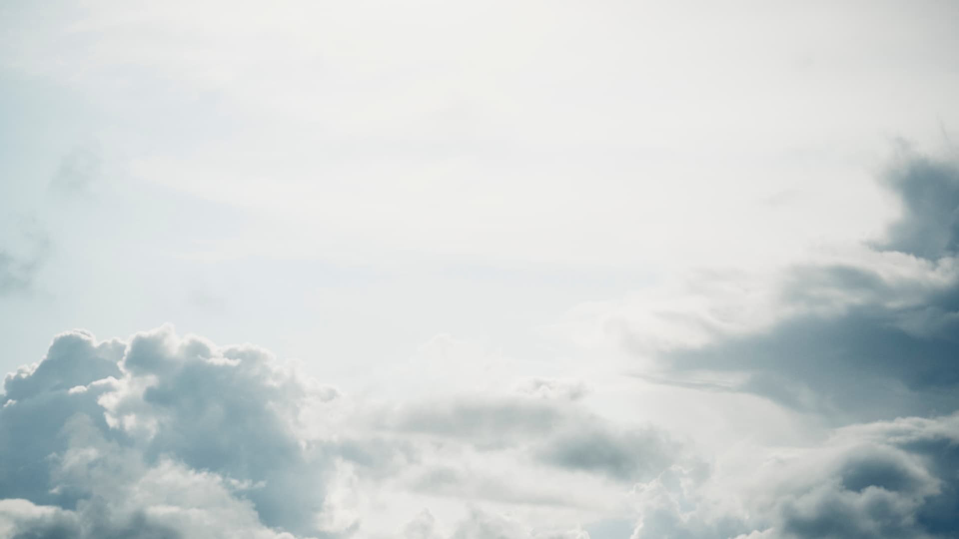En lys, overeksponert himmel med myke, luftige skyer spredt langs bunnen og høyre side av bildet, noe som skaper en rolig og fredfull atmosfære.