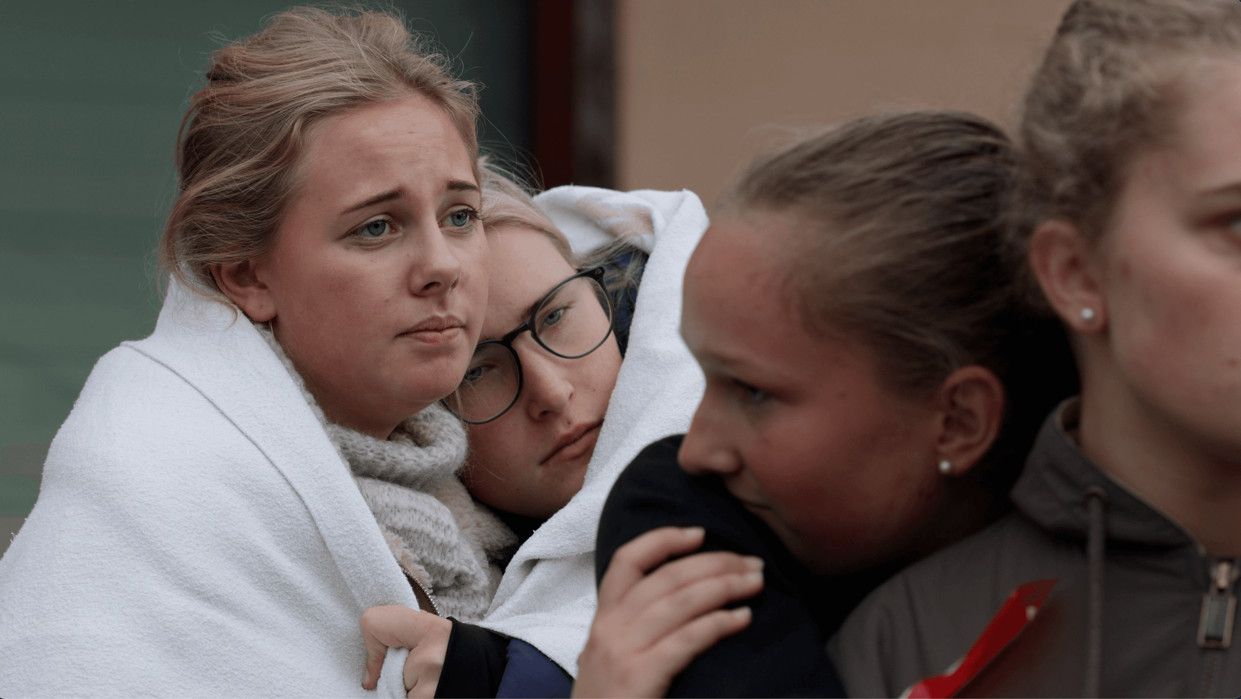 Fire unge kvinner står tett sammen, to av dem pakket inn i hvite tepper. En ser bekymret ut, en annen hviler hodet på skulderen til en venninne, mens to andre ser dystre og bekymrede ut.