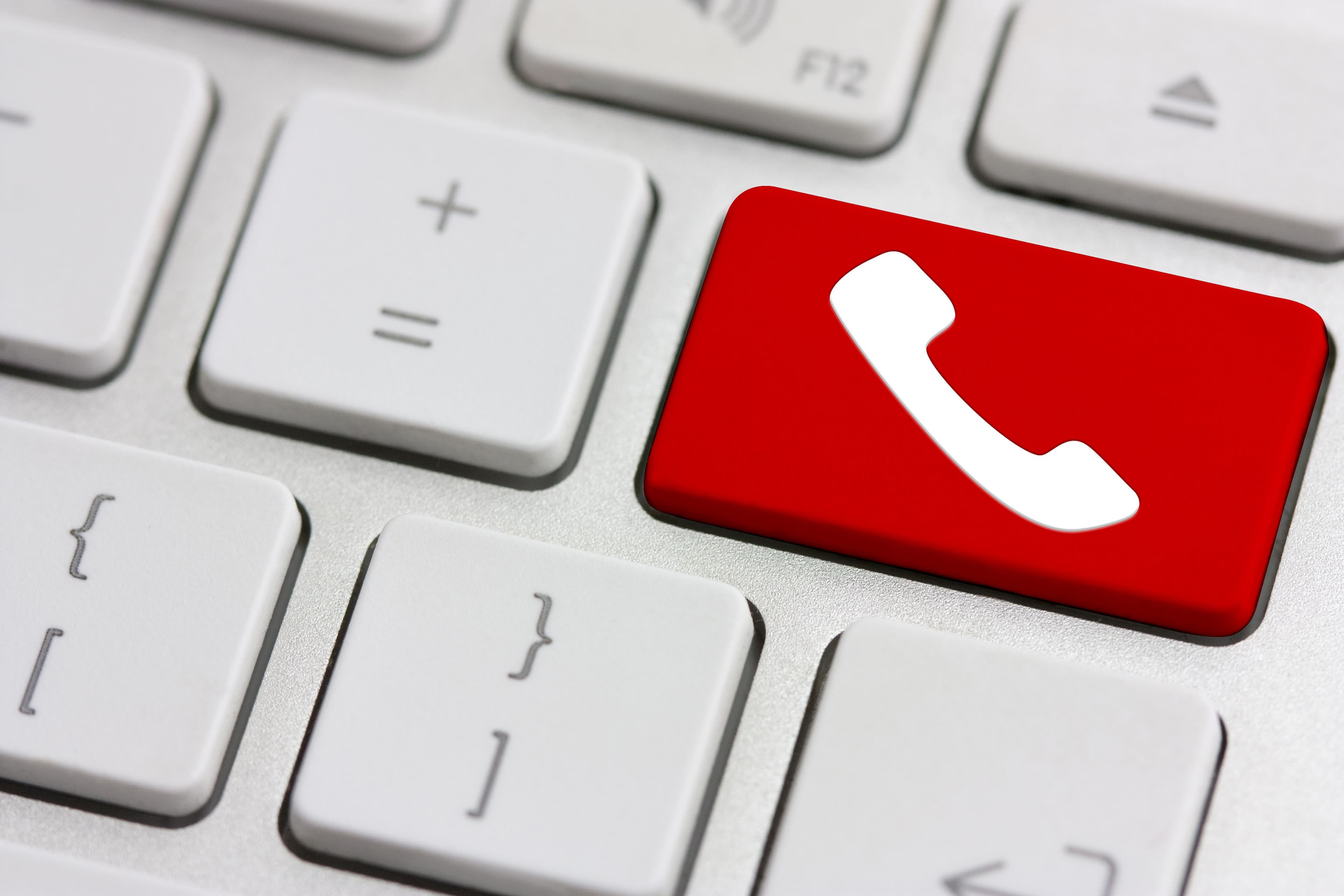 Nærbilde av et datatastatur med en rød tast med et hvitt telefonikon, som symboliserer en samtalefunksjon, omgitt av vanlige hvite taster.