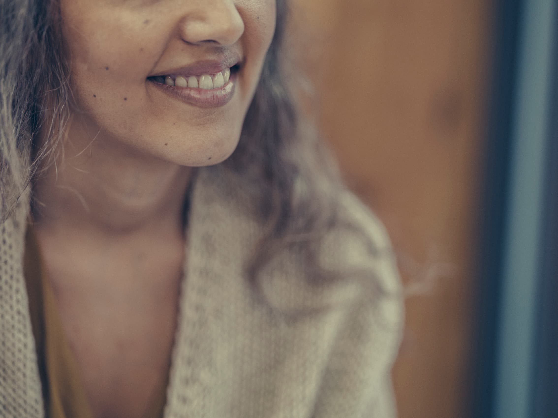 Nærbilde av en kvinne som smiler varmt, og viser bare nedre halvdel av ansiktet. Hun har på seg en kremfarget strikkegenser, og bakgrunnen er svakt uskarp.