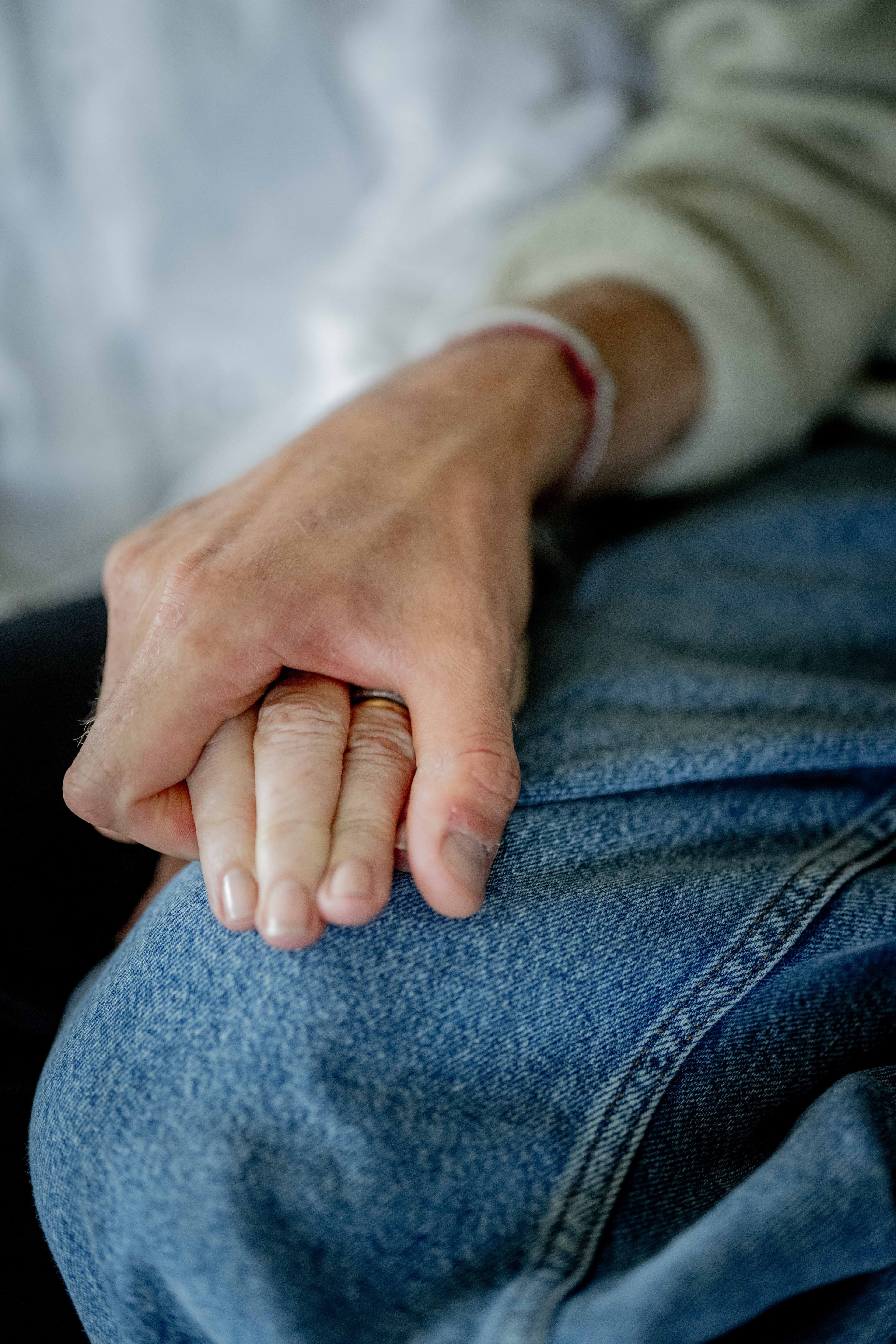 Nærbilde av to hender som forsiktig holder om hverandre, den ene hvilende på et denimkledd ben. Hendene ser ut til å tilhøre personer i ulike aldre, noe som tyder på trøst og støtte.